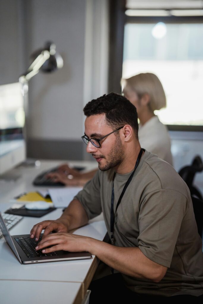Two professionals working diligently at office desks, focusing on tasks using laptops and computers.